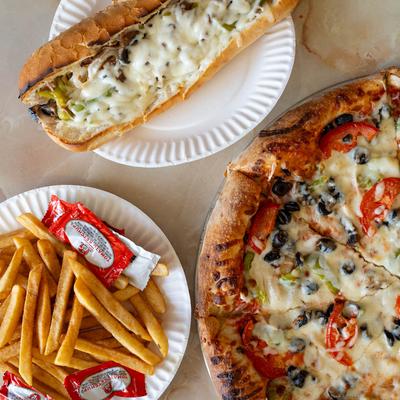 Philly cheesesteak sub sandwich, fries, and vegetarian pizza on a table.