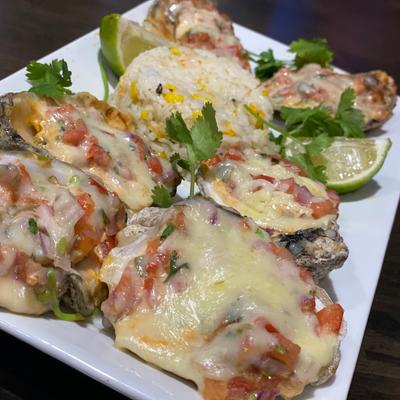 Baked oysters topped with melted cheese and salsa, served with rice and lime wedges.