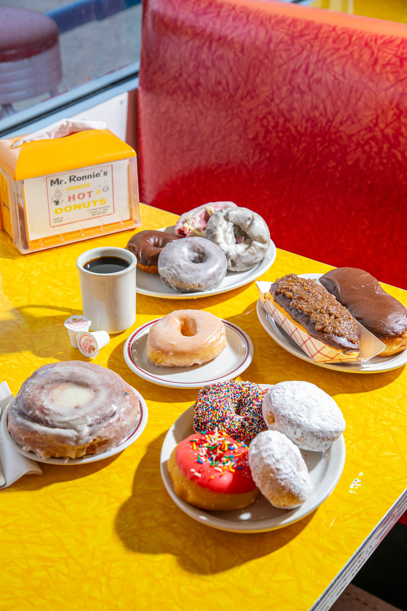 Assortment of donuts and coffee on a yellow diner table with a red seating background