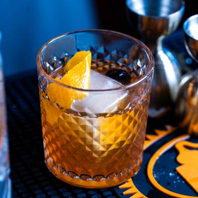 Whisky cocktail served in a crystal tumbler with a large ice cube and an orange peel.