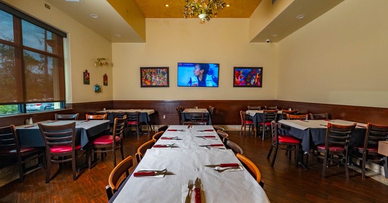 Inside, dining area with tables and chairs, a large window, and a television on the wall