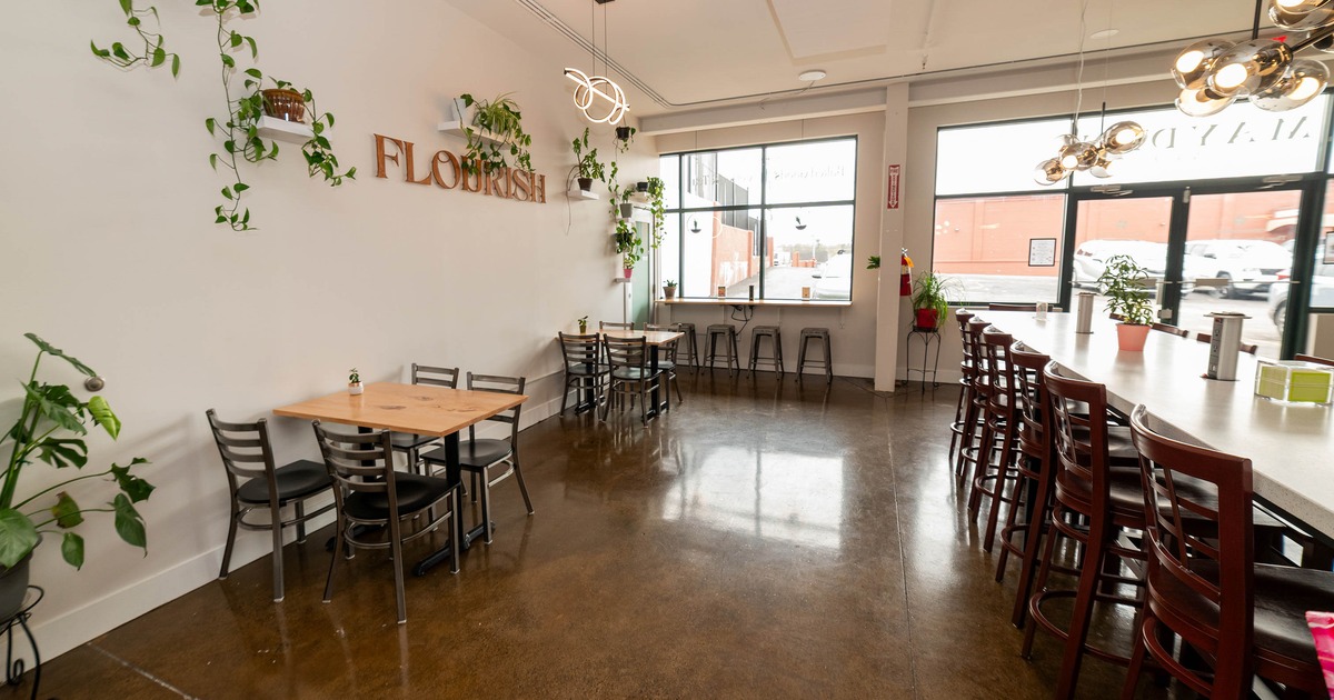 Interior of a modern café with plants, tables, bar counter, and large windows