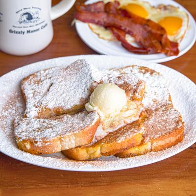 French toast dusted with sugar and topped with butter, alongside fried eggs, bacon and coffee.