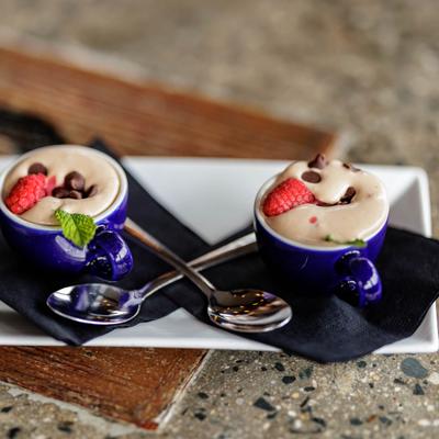 Two blue cups with creamy dessert, garnished with raspberries and chocolate chips.