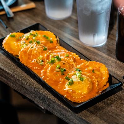 Kimchi ravioli in creamy, orange sauce, garnished with green onions and grated cheese.