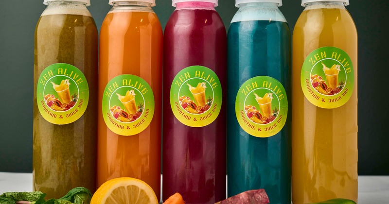 Various bottles of cold-pressed juices alongside fresh fruits and vegetables