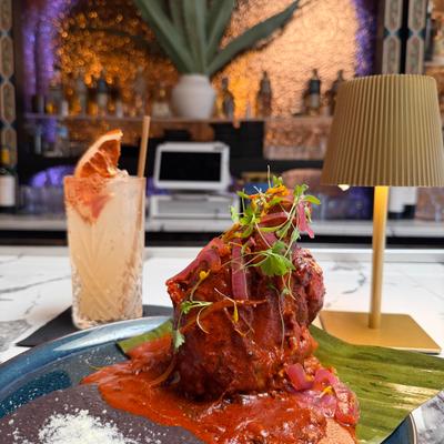 Braised Mexican pork shank in red sauce, paired with a citrus cocktail.
