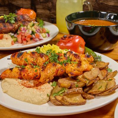 Chicken Kebob Plate on a table with lamb kebob plate, lentil soup, and a lemonade.