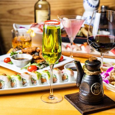 Green sparkling cocktail on a table with sushi rolls and assorted Japanese dishes.