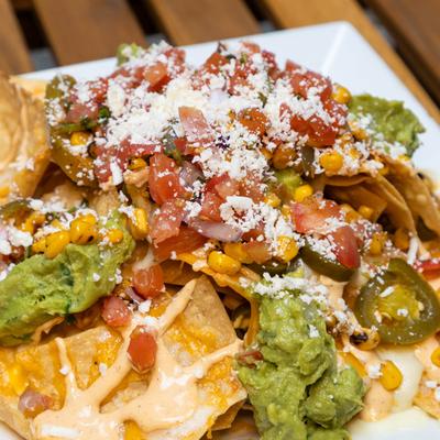 Nachos, with refried beans, salsa, guacamole, roasted corn, jalapenos, and cheeses.