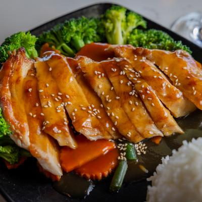 Chicken teriyaki  with broccoli, carrot, and rice on a black plate.