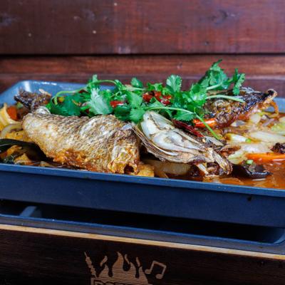 Spicy whole fish with vegetables, dried chilies, and cilantro served on a metal tray.