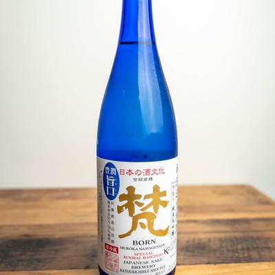 A blue bottle of Muroka Nama Genshu sake on a wooden surface, against white background.