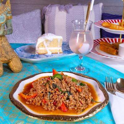 Pad Gra Pow served on the plate with a drink and a slice of cake.