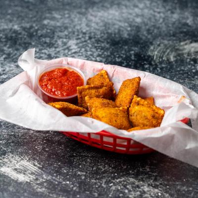A basket filled with toasted raviolis and a tomato-based sauce for dipping.
