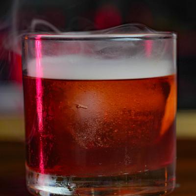 Cocktail in a rocks glass with smoke coming out of the glass.
