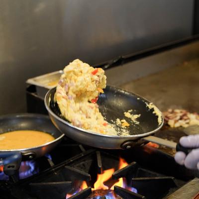 Ham and pepper scrambled eggs cooking in a skillet over an open flame.