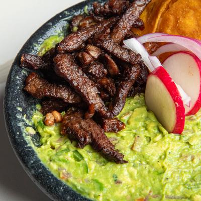 Deep-fried ribeye steak served over a bed of creamy guacamole, close-up.