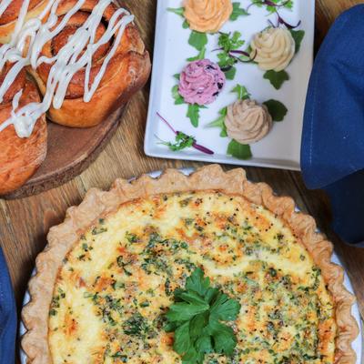 Quiche garnished with parsley beside a plate of cinnamon rolls.