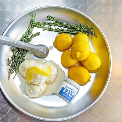 A metal tray with scoops of ice cream, rosemary sprigs, lemons, and a jar labeled salt.