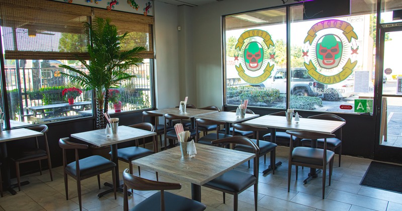 Interior with tables, chairs and large windows with a luchador theme.