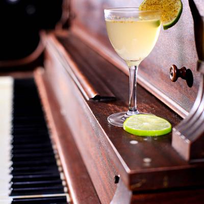 Cocktail in Nick and Nora glass, garnished with lime wheels, resting on a piano.