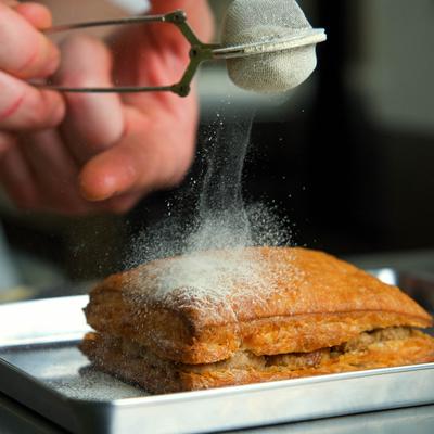 Close-up of powdered sugar being dusted over a layered puff pastry on a tray.