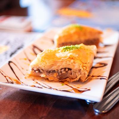 Baklava slice topped with crushed pistachios and drizzled with chocolate.