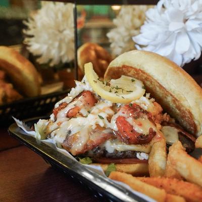 A seafood burger topped with shrimp, crab, and cheese, served with fries.