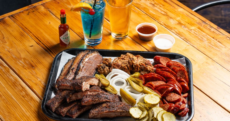 A tray of ribs, pulled pork, and sausage slices, served with drinks