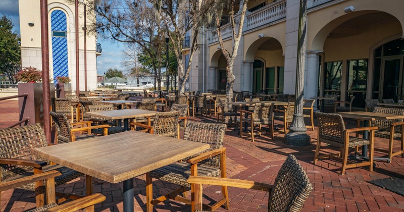 Outdoor cafe with empty wooden tables and wicker chairs on red brick patio