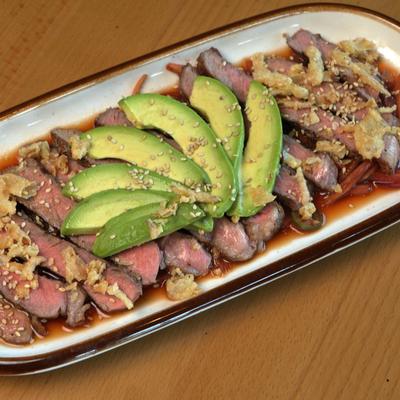 Ribeye steak strips in red sauce, topped with guacamole and sesame seeds.