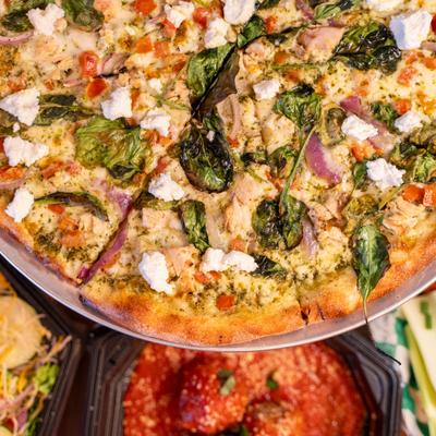 Pesto Supremo Pizza alongside a dish of meatballs in tomato sauce below the pizza.
