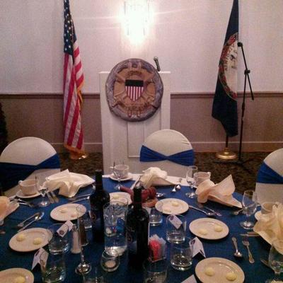 Formal banquet table arrangement with podium, American and state flags, and wine bottles.
