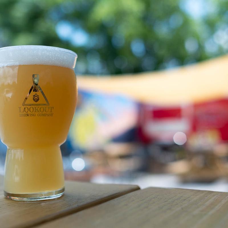 Glass of craft beer branded with the brewery's sign, served on a outdoor table.