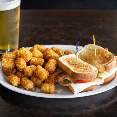 BLT sandwich with a side of tater tots, served beside a glass of beer.