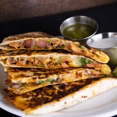 Close-up of a stack of quesadilla slices filled with chicken, with sauces on the side.