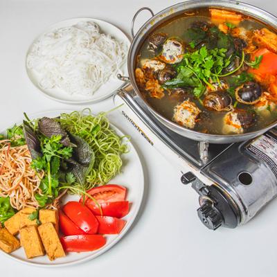 Vietnamese hot pot served with rice noodles, tofu, tomatoes, and fresh herbs.