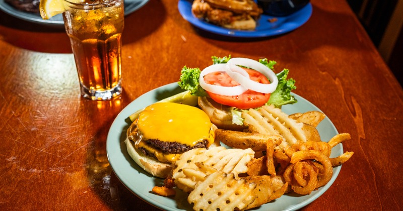 Cheseburger with fries served on the table with a drink
