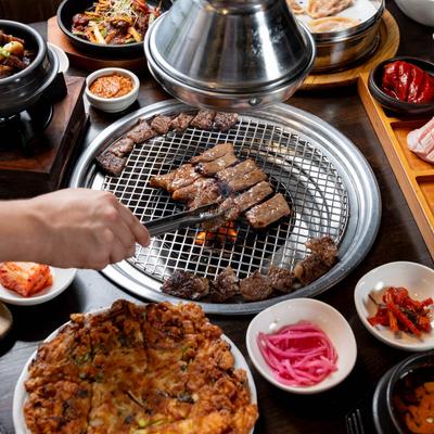A hand moving meat on the grill with tongs.