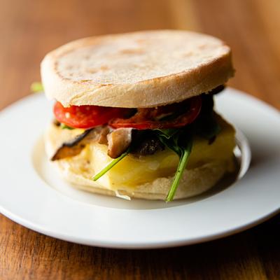 An english muffin sandwich with mushroom, tomato, spinach, egg and cheese.