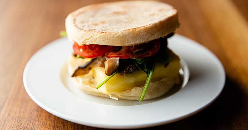 An english muffin sandwich with mushroom, tomato, spinach, egg and cheese