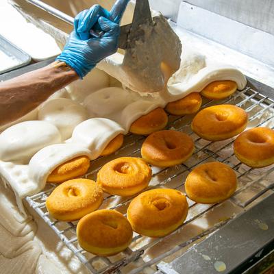 A baker uses a tool to cover freshly baked golden donuts with white icing.