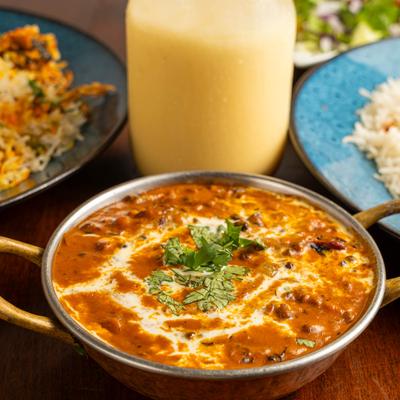 A bowl of Dal Makhani served alongside rice and a Mango Lassi.