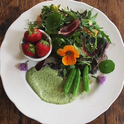Salad with mixed greens, snap peas, strawberries, edible flowers and dressing.