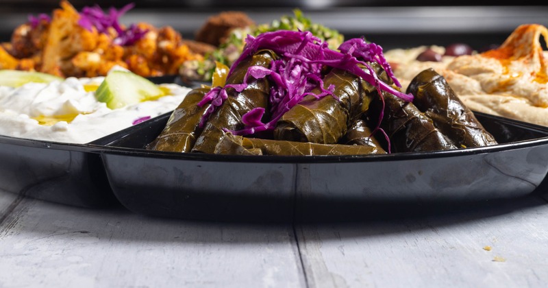 A black platter with stuffed grape leaves, surrounded by creamy dips