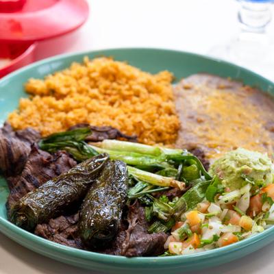 Carne asada plate with rice, beans, salad, and blistered peppers.