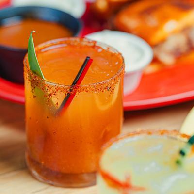 Spicy orange cocktail with chili rim and leaf garnish.