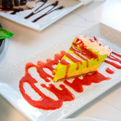 A slice of key lime pie with strawberry sauce on a white plate.