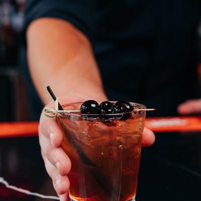 A hand holding Manhattan cocktail on the rocks with cherry garnish.